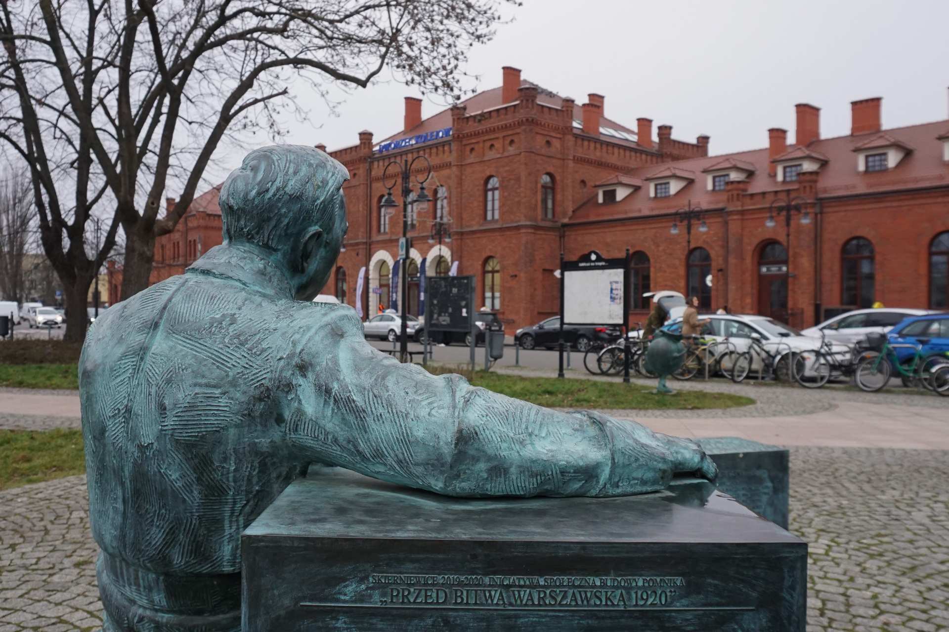 Na pierwszym planie pomnik. W tle dworzec w Skierniewicach.